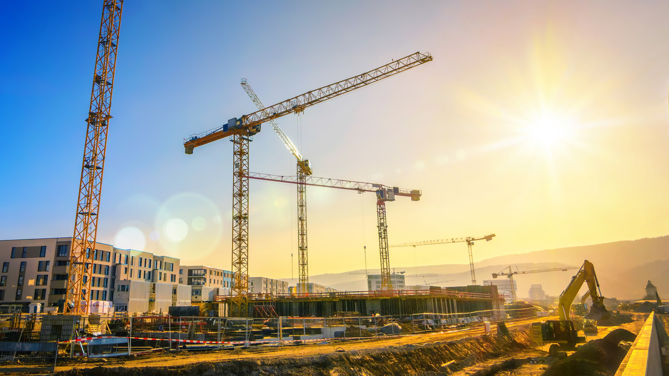 Large construction site including several cranes, with clear sky and the sun, construction consultant